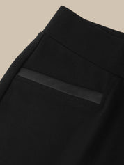 Close-up of a black garment, likely a skirt or dress, showing a structured waistband and a horizontal satin-like band detail across the front, set against a solid beige background.