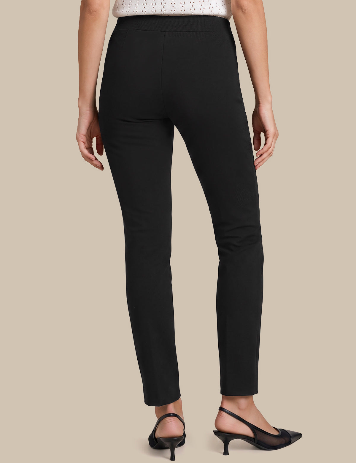 A model shown from the back wearing slim black ankle-length pants, a white knit top, and black slingback heels against a solid beige background.