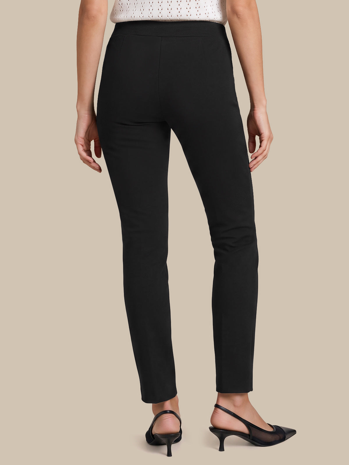 A model shown from the back wearing slim black ankle-length pants, a white knit top, and black slingback heels against a solid beige background.