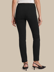 A model shown from the back wearing slim black ankle-length pants, a white knit top, and black slingback heels against a solid beige background.
