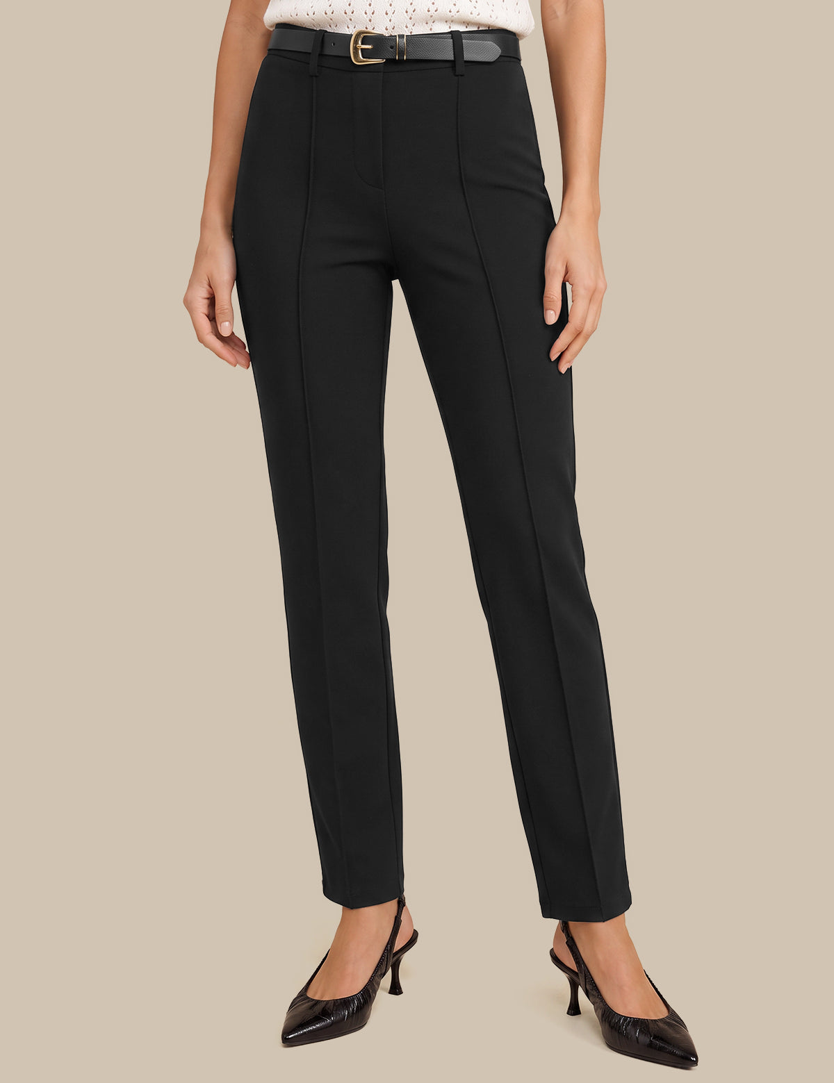 A model wearing a pair of black high-waisted, straight-leg trousers with a matching black belt, styled with a white top and black pointed-toe heels against a solid beige background.