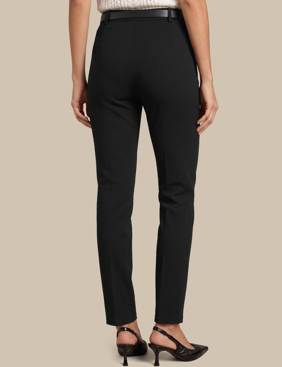 Rear view of a model wearing black slim-fit trousers with a black belt, paired with black slingback heels, against a solid beige background.
