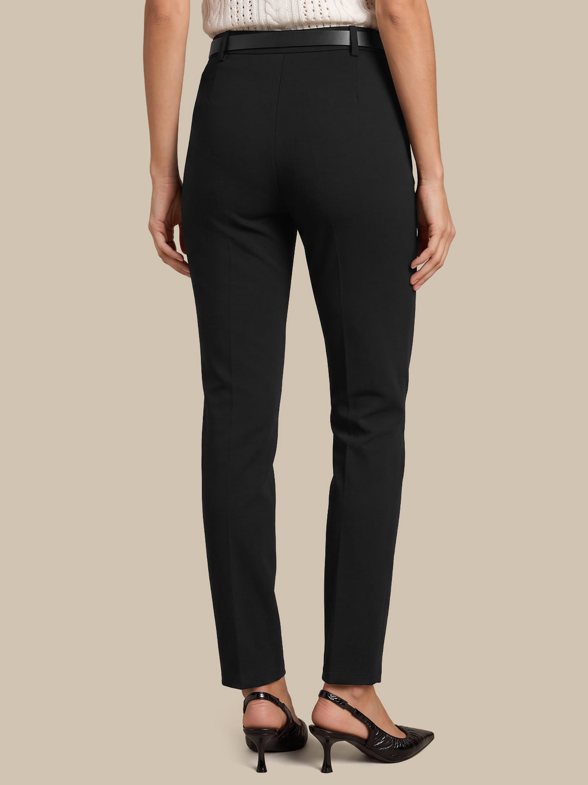 Rear view of a model wearing black slim-fit trousers with a black belt, paired with black slingback heels, against a solid beige background.