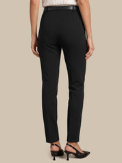 Rear view of a model wearing black slim-fit trousers with a black belt, paired with black slingback heels, against a solid beige background.