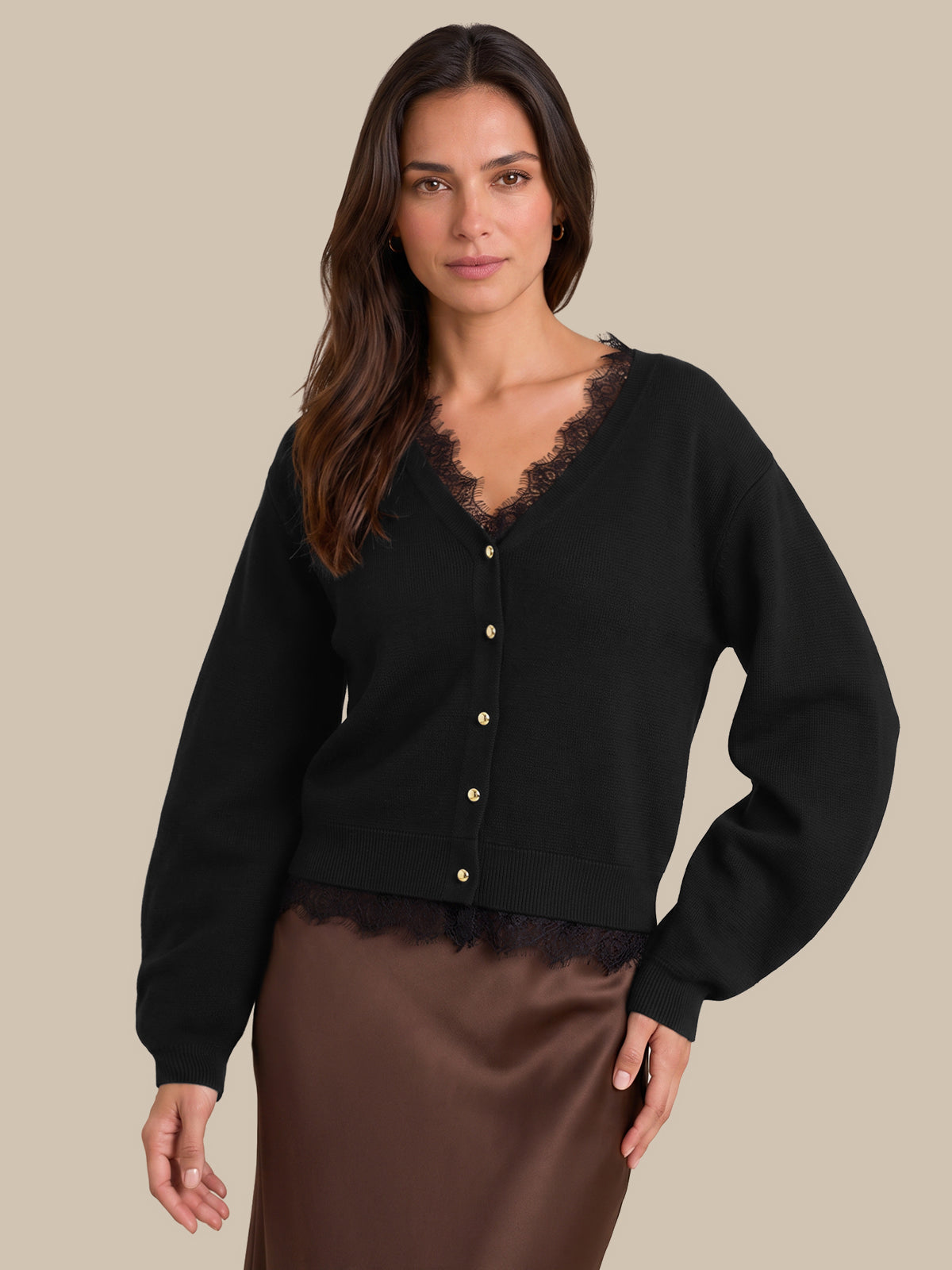 A woman modeling a black cardigan with gold buttons and a black lace V-neck trim, paired with a brown satin skirt, against a solid beige background.