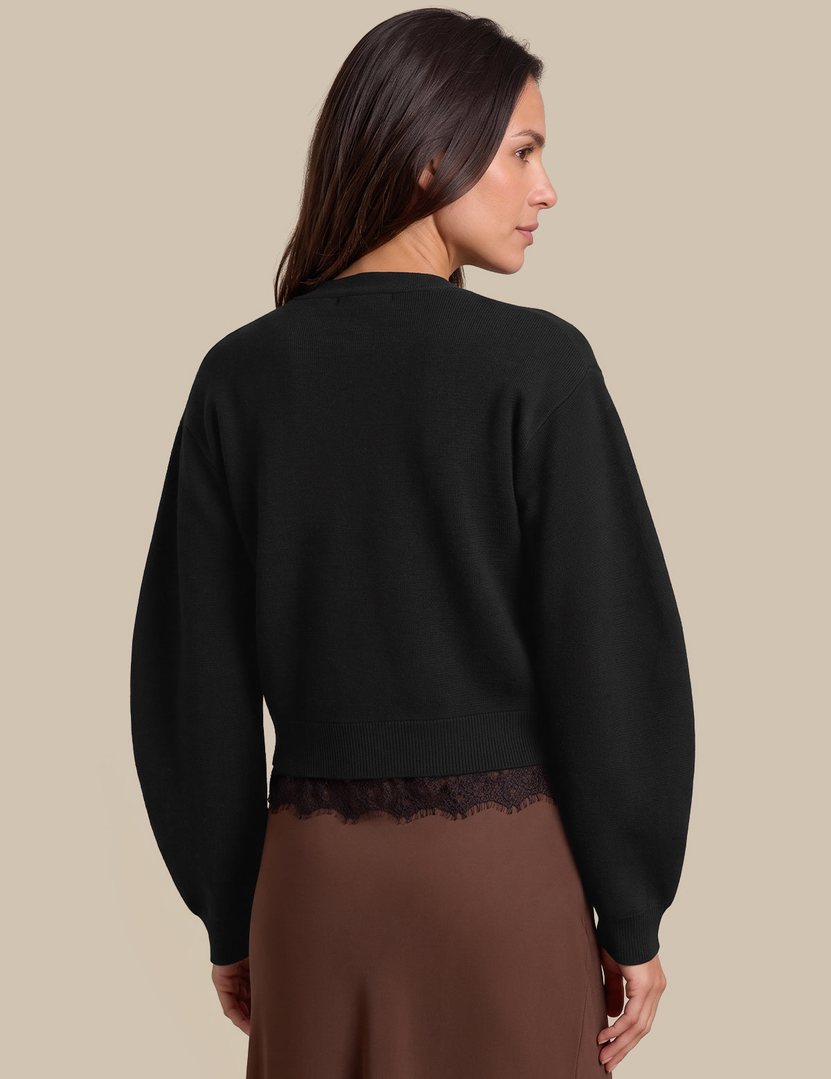 A woman shown from the back wearing a black cropped crewneck sweatshirt with a lace hem and a brown skirt, set against a solid beige background.