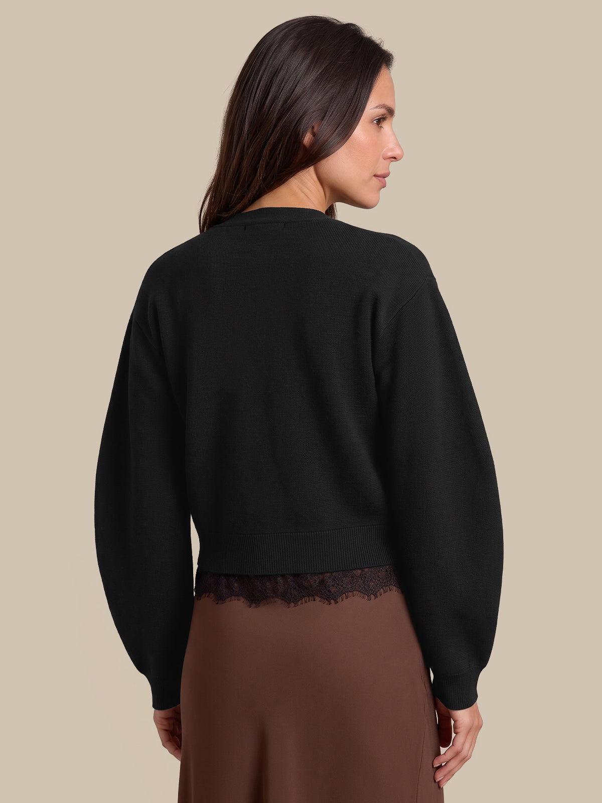 A woman shown from the back wearing a black cropped crewneck sweatshirt with a lace hem and a brown skirt, set against a solid beige background.