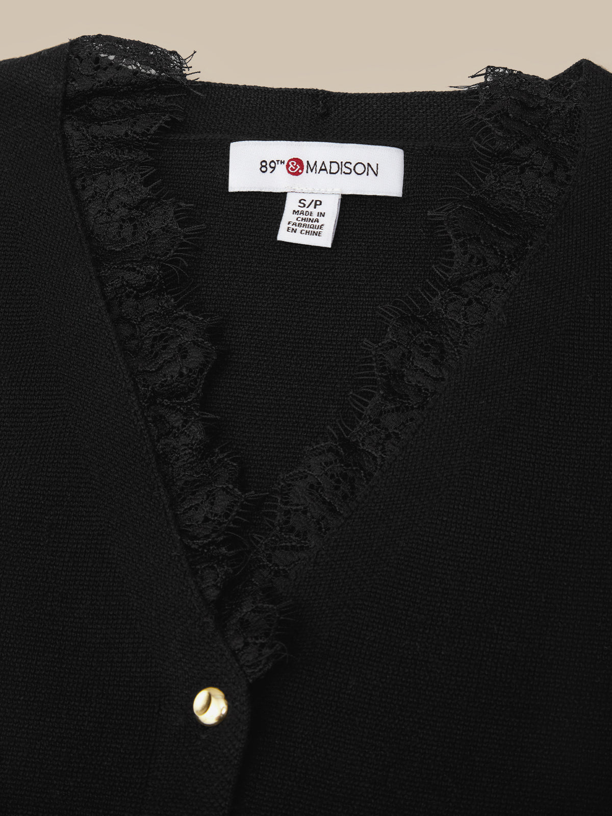 Close-up of a black knit cardigan with a V-neck and frayed lace trim, featuring a white interior neck label that reads 89° MADISON.