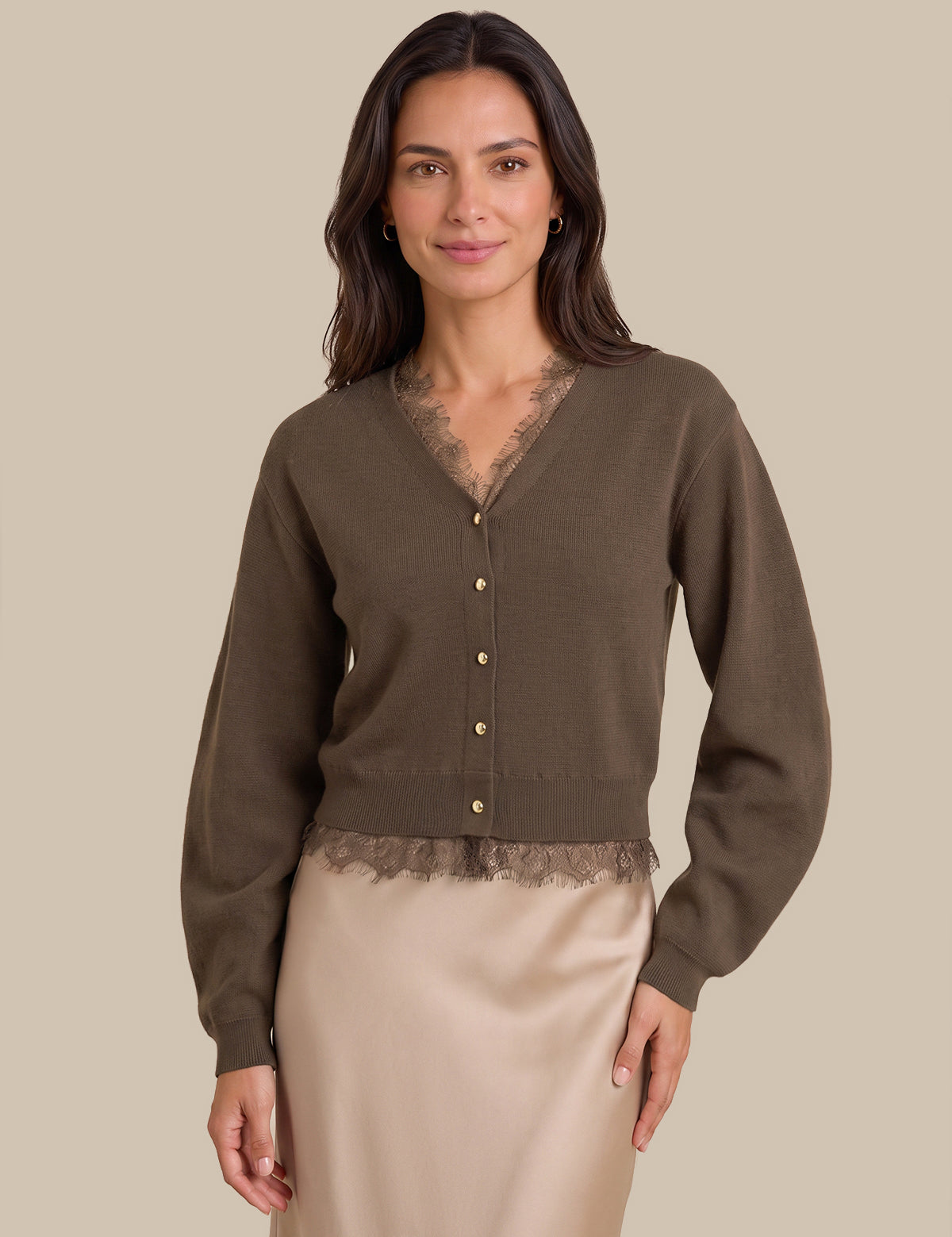 A woman modeling a dark brown cardigan with a lace V-neck and button-front detail, paired with a beige satin skirt, against a solid beige background.