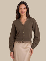A woman modeling a dark brown cardigan with a lace V-neck and button-front detail, paired with a beige satin skirt, against a solid beige background.