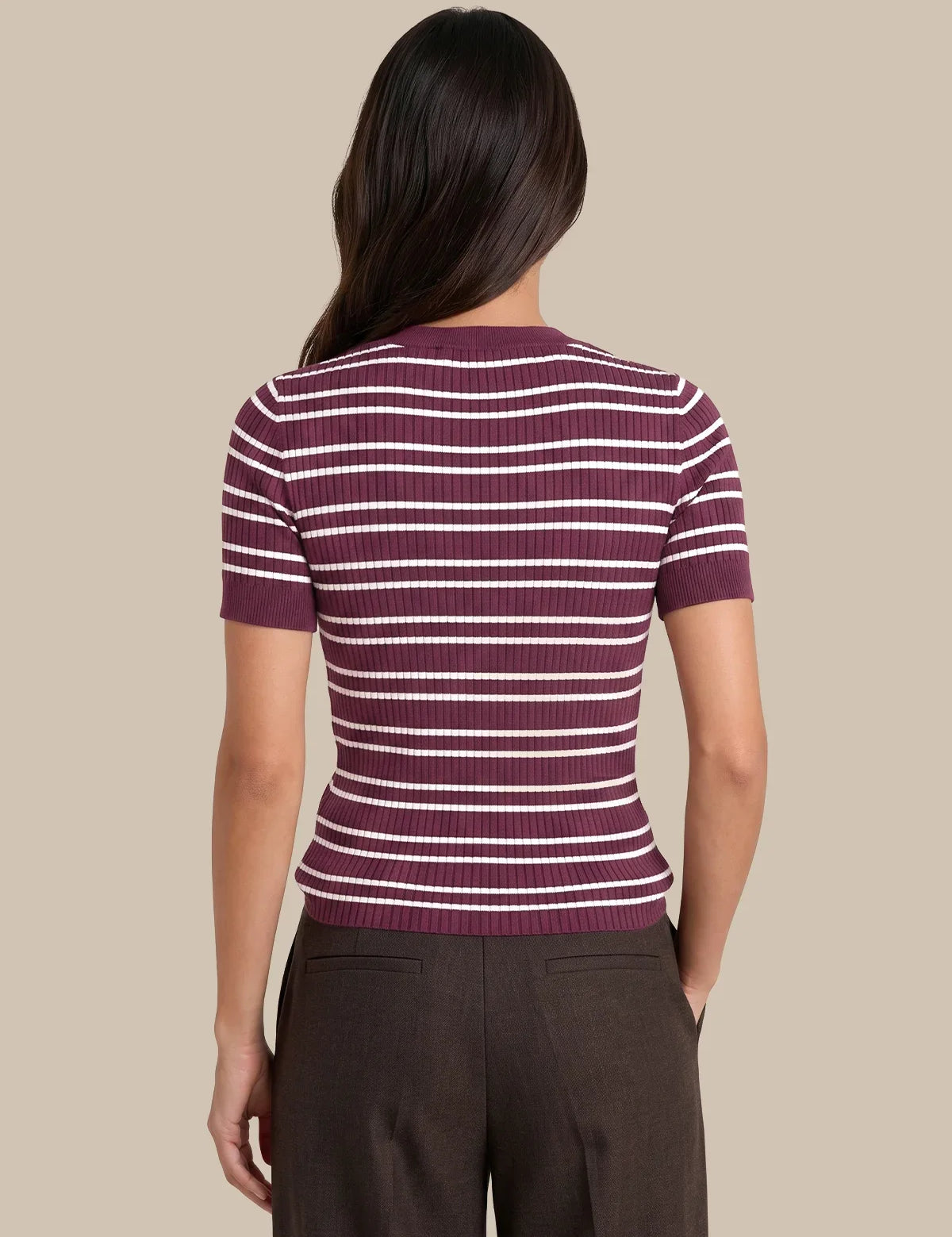A woman shown from the back wearing a short-sleeve ribbed knit top with horizontal burgundy and white stripes, paired with dark brown trousers, against a solid beige background.