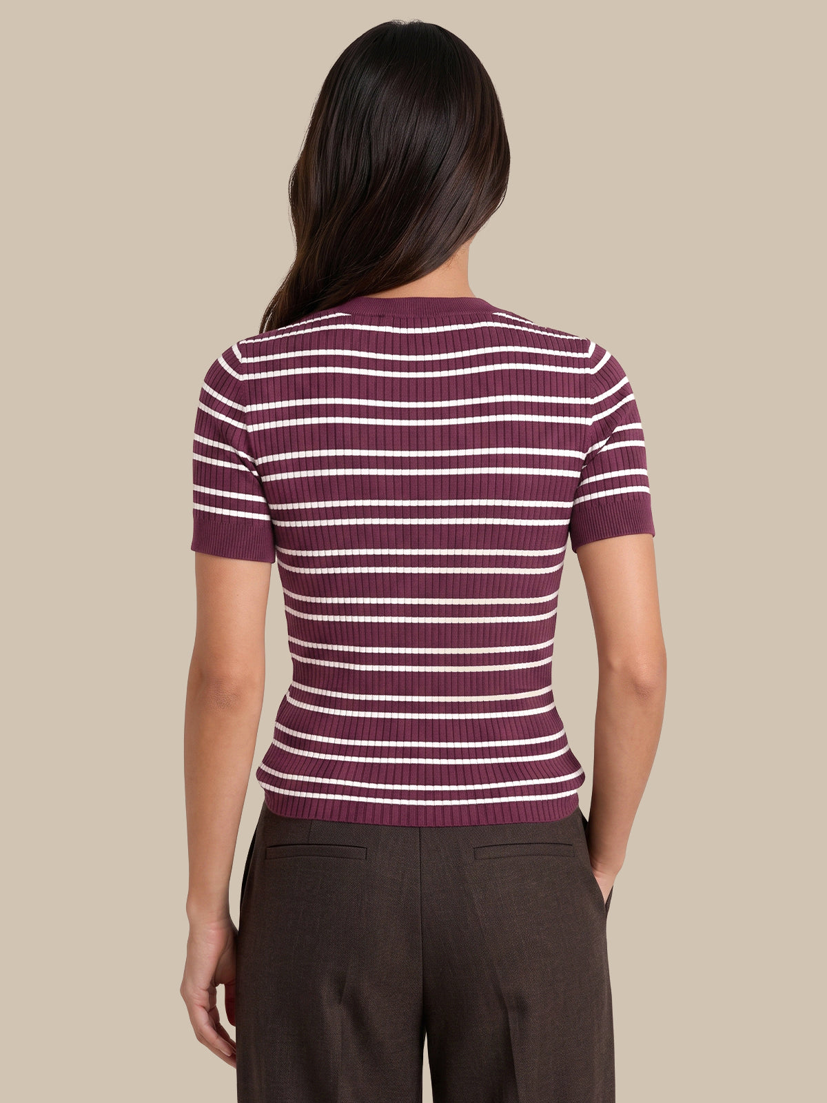 A woman shown from the back wearing a short-sleeve ribbed knit top with horizontal burgundy and white stripes, paired with dark brown trousers, against a solid beige background.