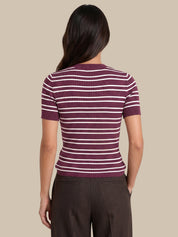 A woman shown from the back wearing a short-sleeve ribbed knit top with horizontal burgundy and white stripes, paired with dark brown trousers, against a solid beige background.