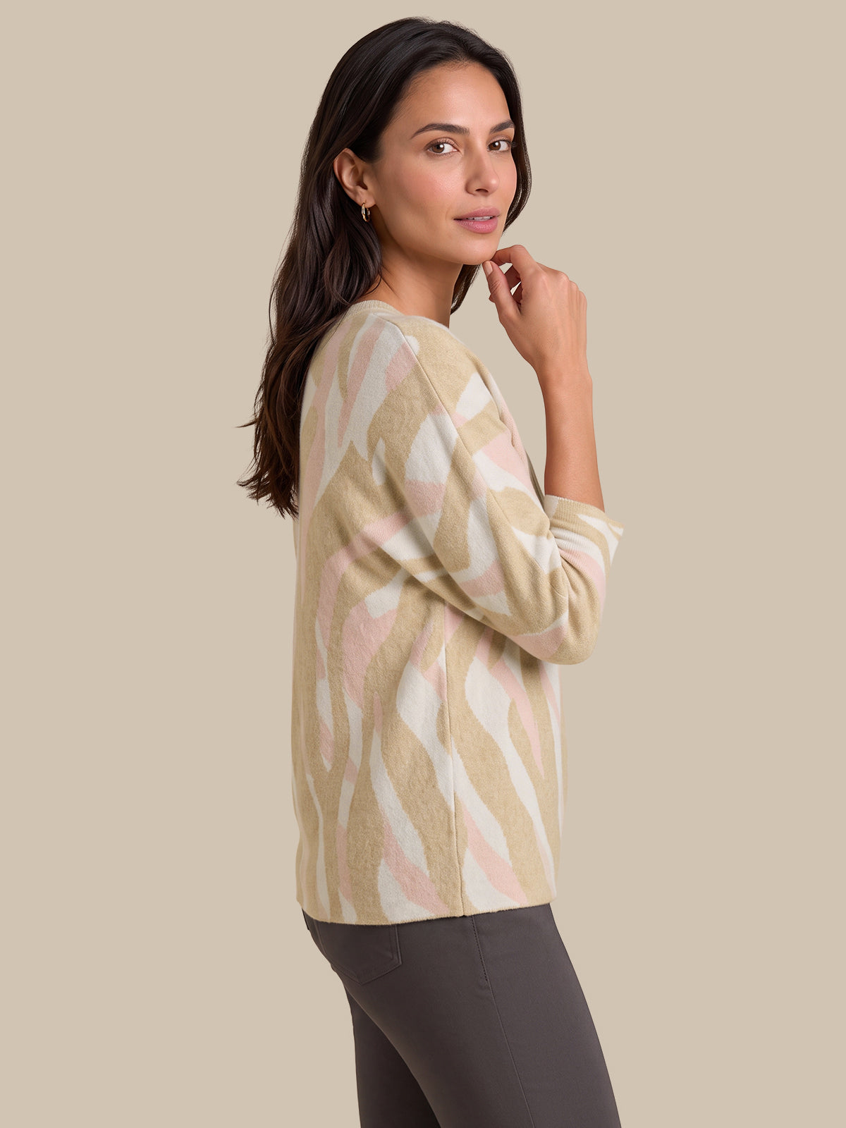 A woman wearing a beige, cream, and light pink abstract patterned knit sweater, paired with dark gray leggings, photographed against a solid beige studio background.
