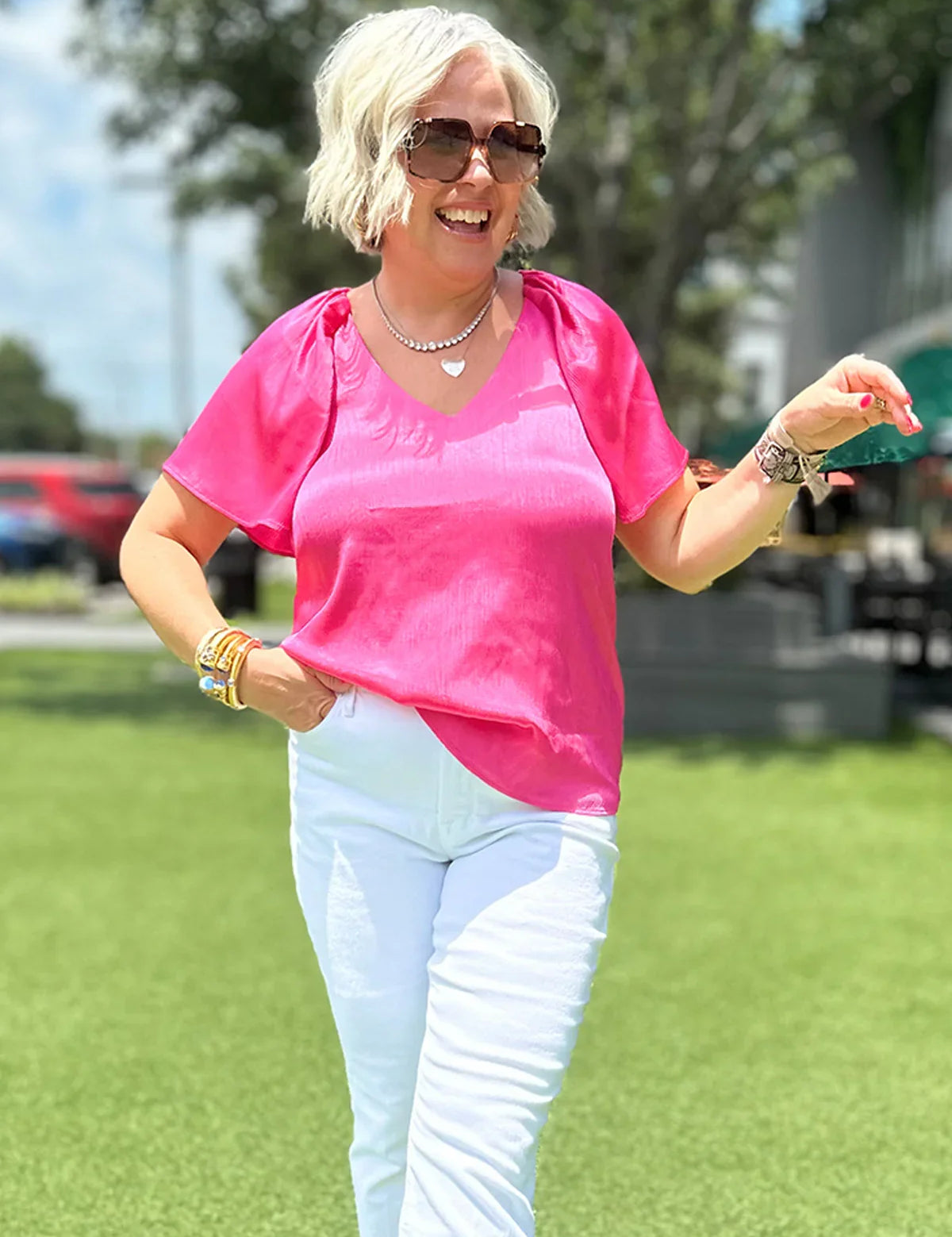 Woman in vibrant pink V-neck top and white pants, styled for effortless everyday wear outdoors