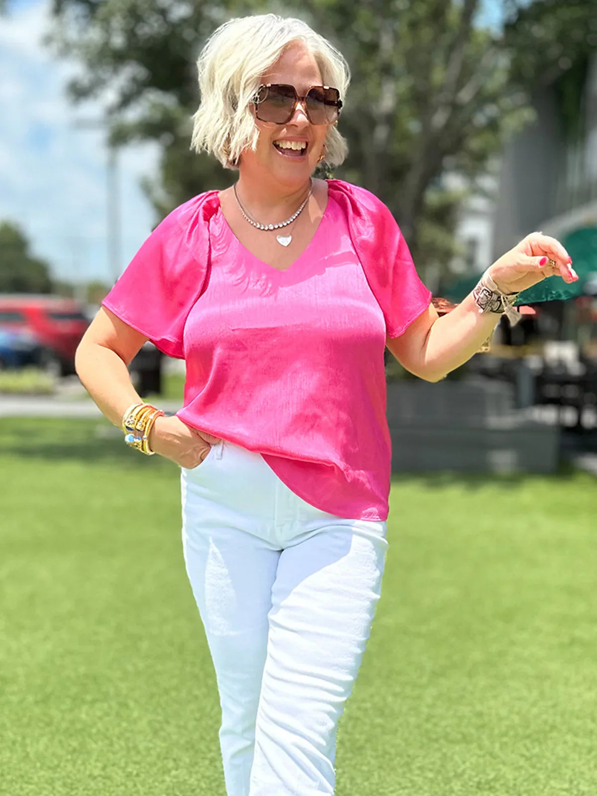 Woman in vibrant pink V-neck top and white pants, styled for effortless everyday wear outdoors