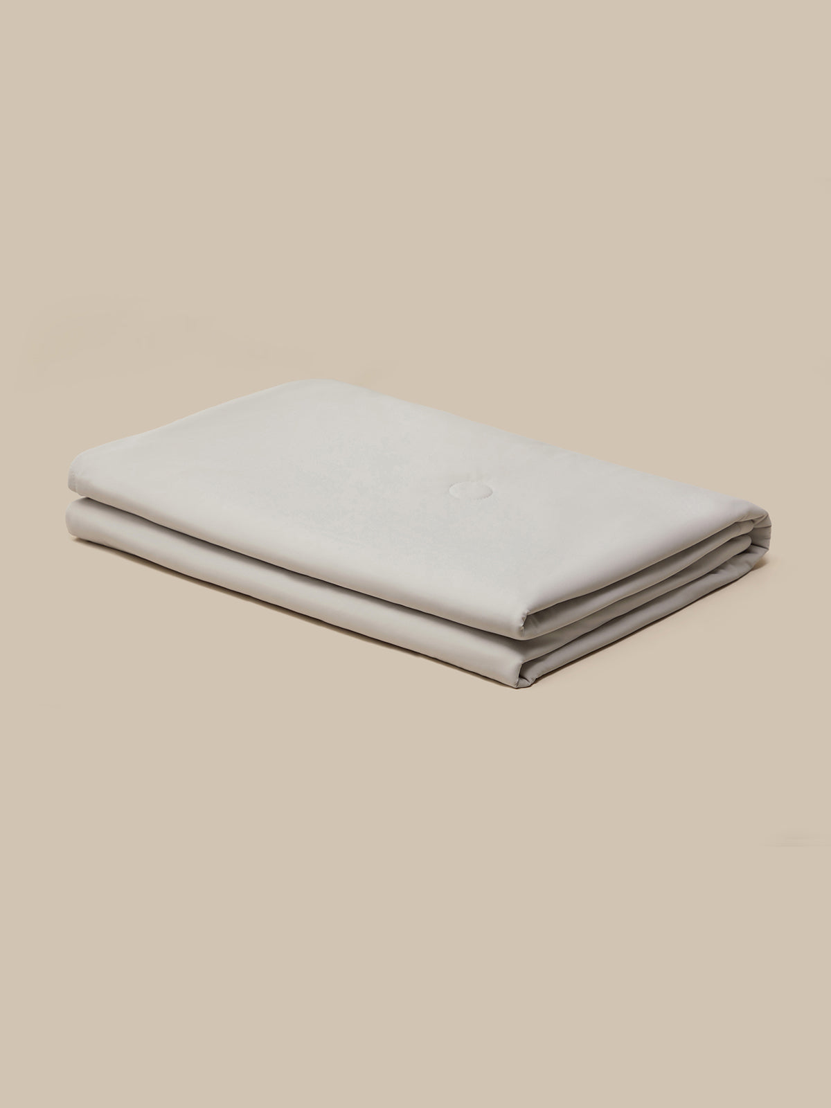 A folded light gray fabric item, likely a blanket or sheet, displayed on a solid beige background.