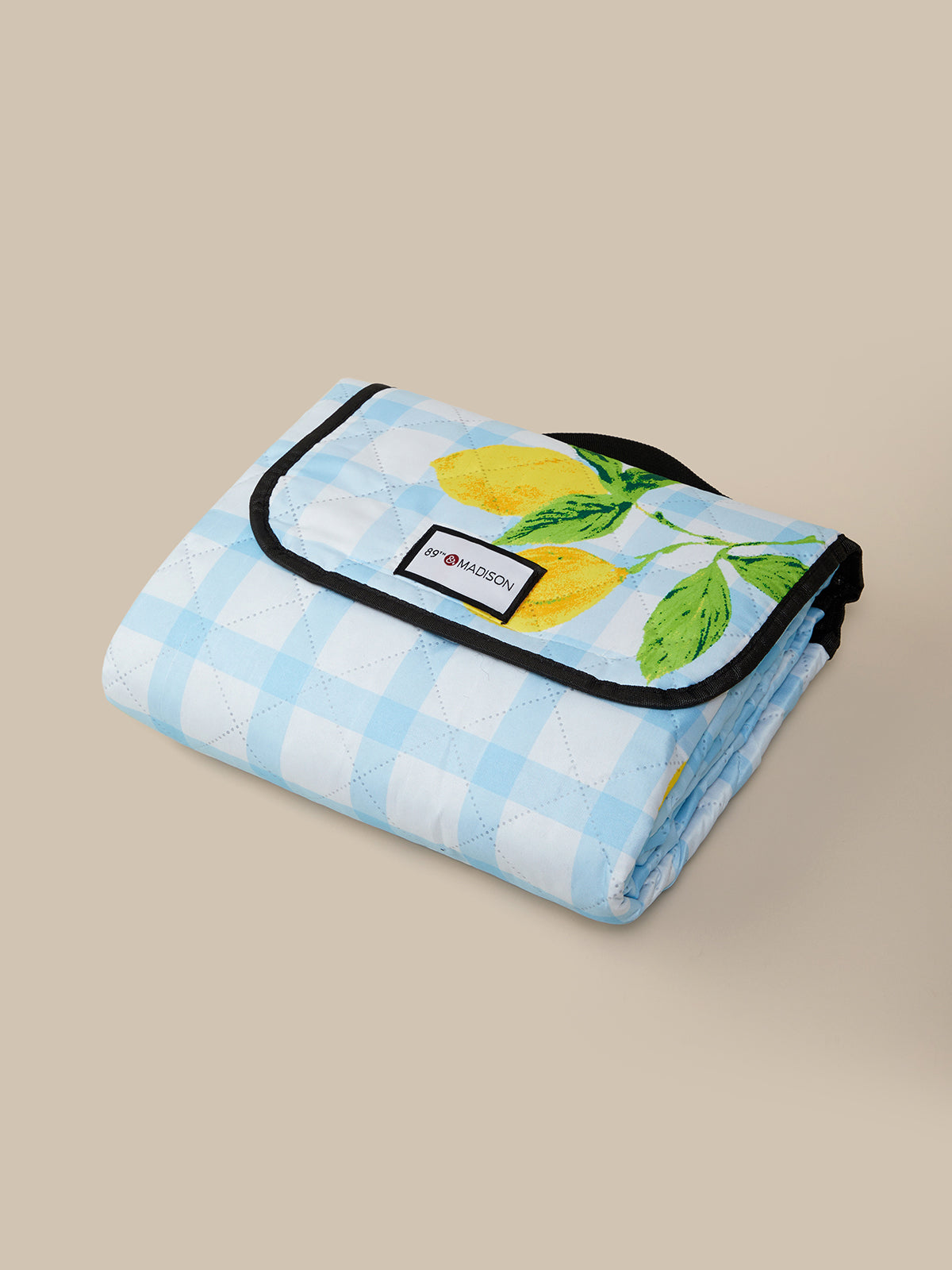 Folded picnic blanket with lemon and mint design on a beige background