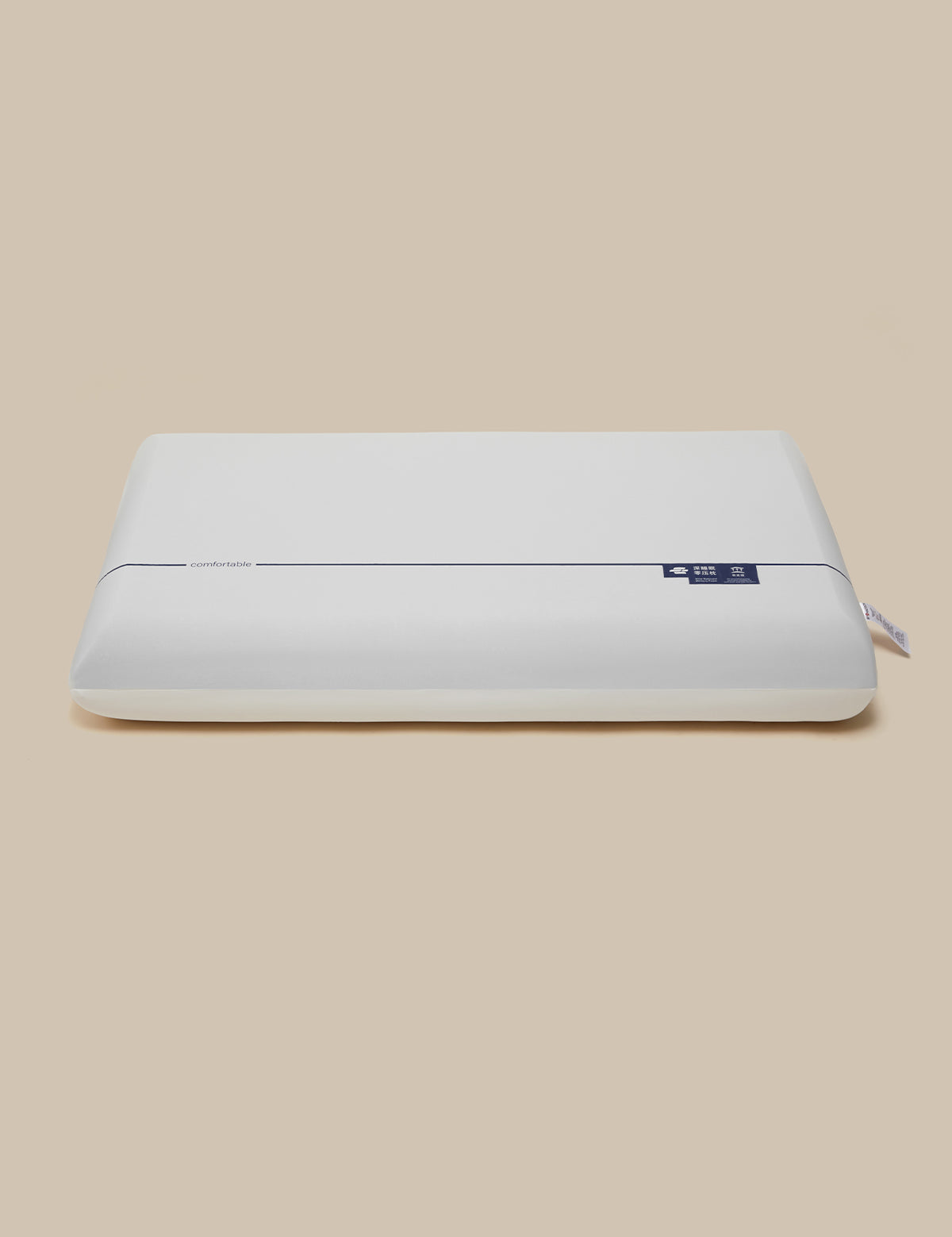 A white rectangular pillow with a smooth, matte finish and a small blue brand tag on the upper right side, set against a solid beige background.