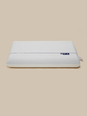A white rectangular pillow with a smooth, matte finish and a small blue brand tag on the upper right side, set against a solid beige background.
