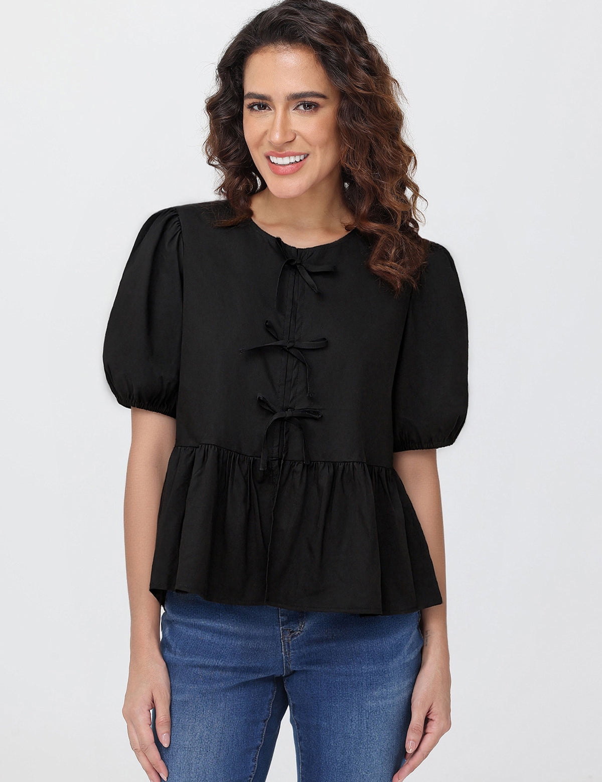 Woman wearing a black blouse with puff sleeves and blue jeans on a white background