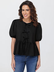 Woman wearing a black blouse with puff sleeves and blue jeans on a white background