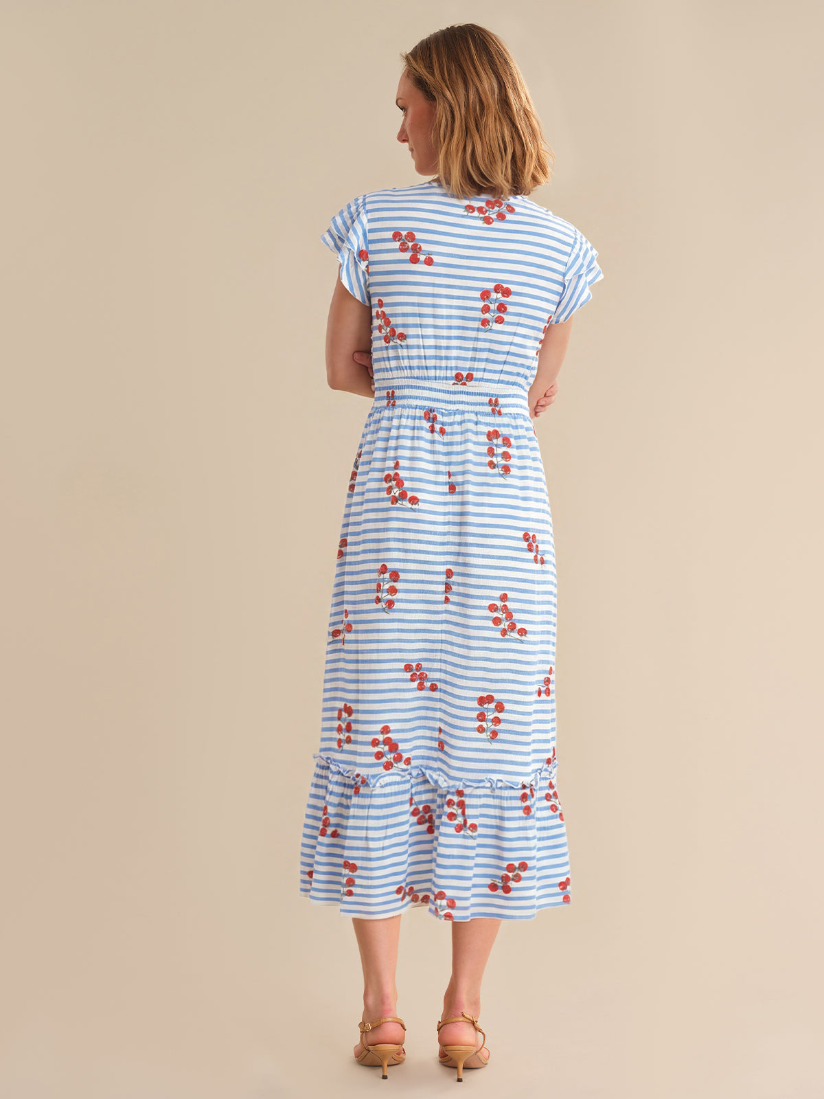 Woman wearing a blue and white striped dress with red floral patterns on a beige background