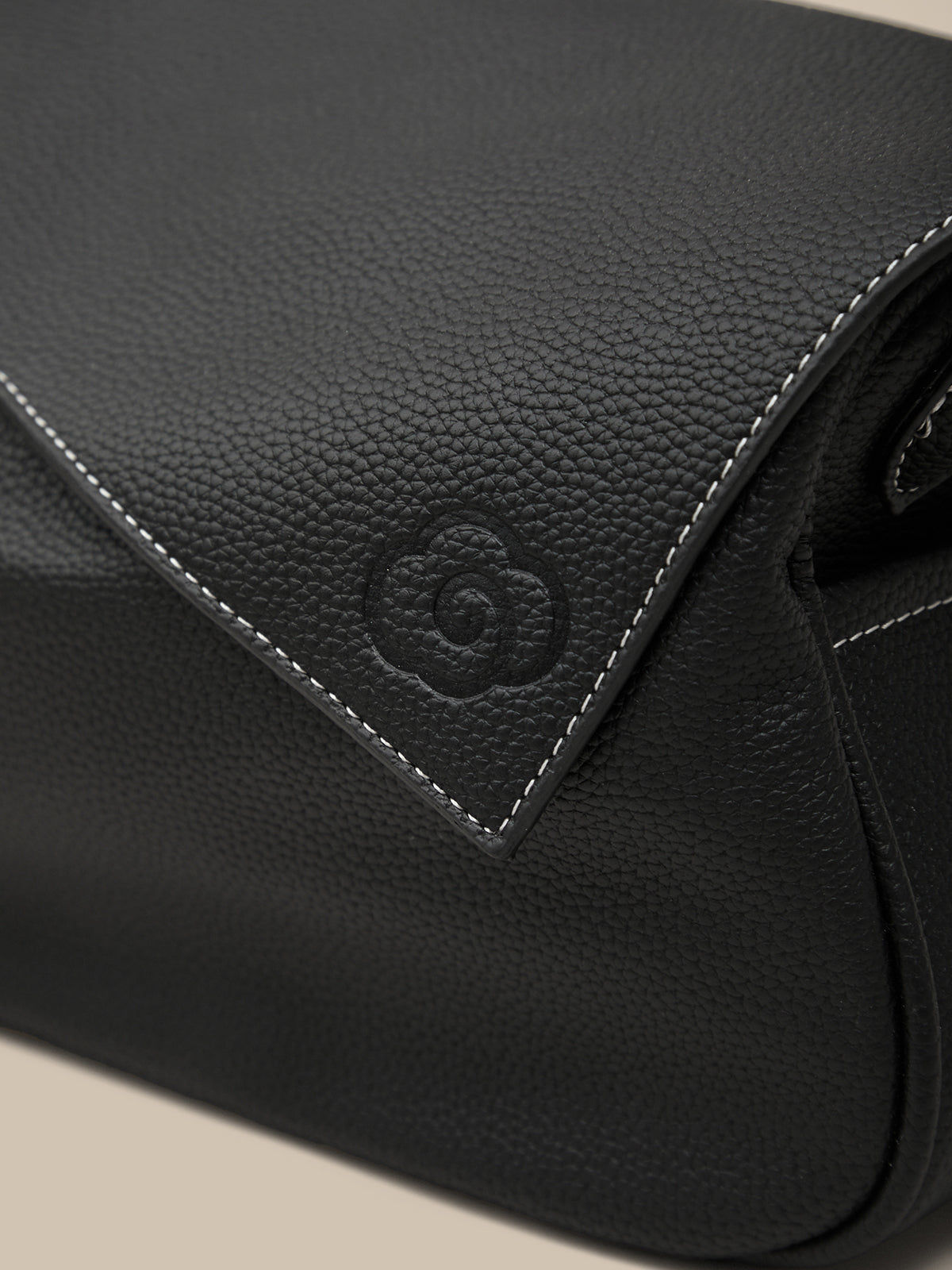 Close-up of a black leather bag with a brand logo on a beige background