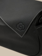 Close-up of a black leather bag with a brand logo on a beige background