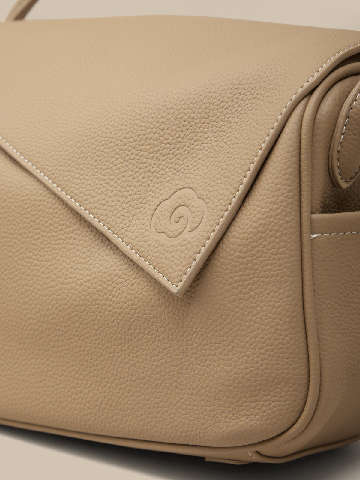 Beige leather handbag with a brand logo on a light background