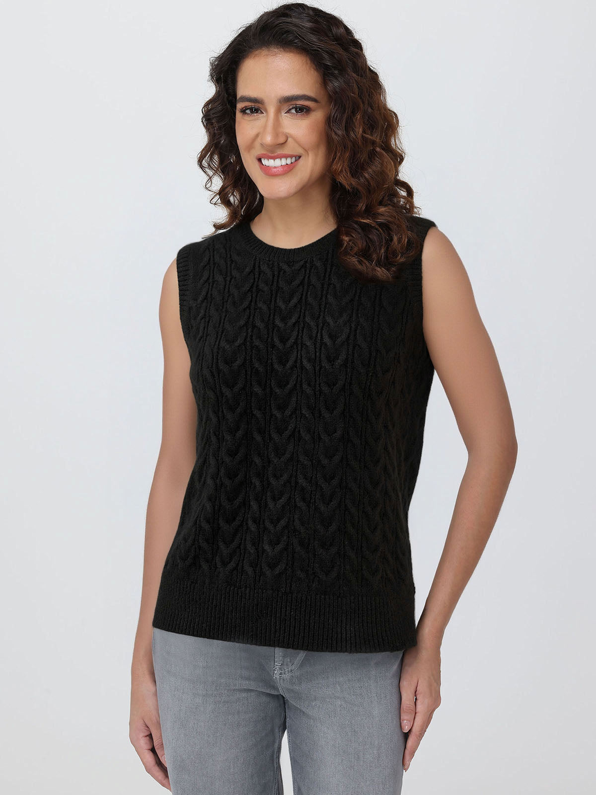 Woman wearing a black sleeveless knitted top against a plain background