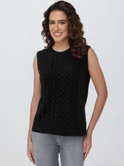 Woman wearing a black sleeveless knitted top against a plain background