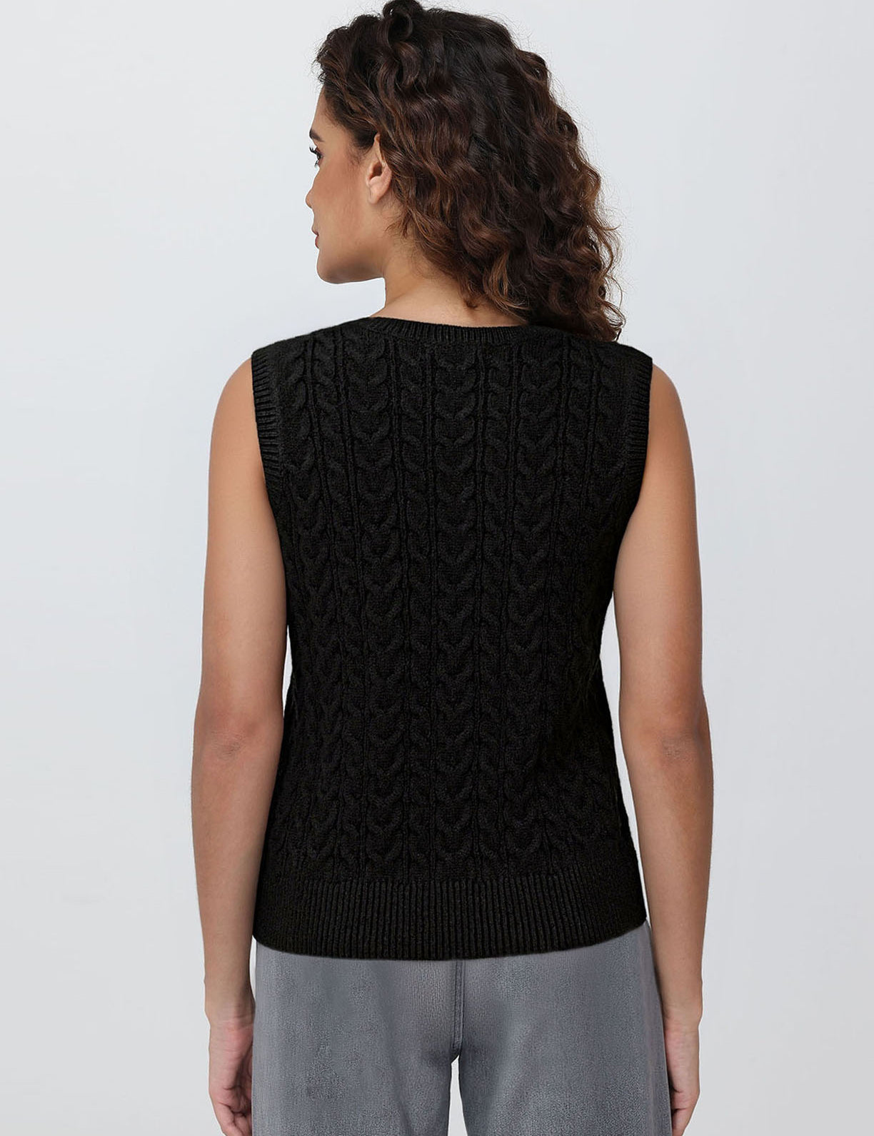 Person wearing a black sleeveless knitted sweater on a plain background