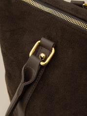 Close-up of a dark brown leather bag with gold hardware on a beige background