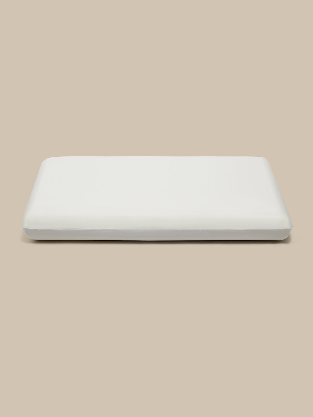 A white rectangular pillow, shown from a top-down view on a solid beige background.