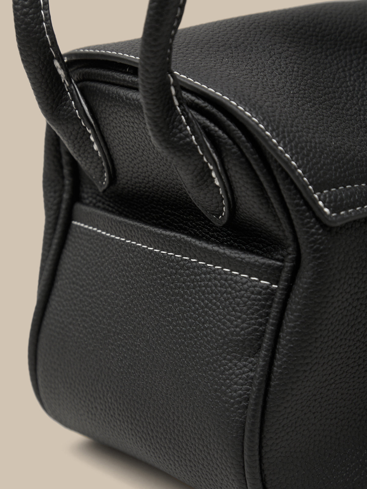 Close-up of a black leather handbag with visible stitching on a beige background