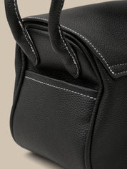 Close-up of a black leather handbag with visible stitching on a beige background