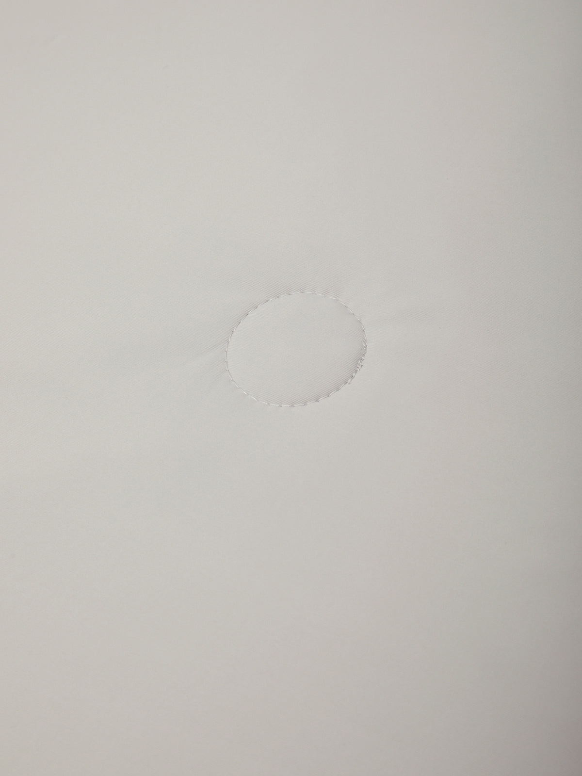 A close-up of a plain white fabric surface with a small circular stitched or dashed detail near the center.