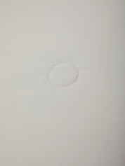 A close-up of a plain white fabric surface with a small circular stitched or dashed detail near the center.