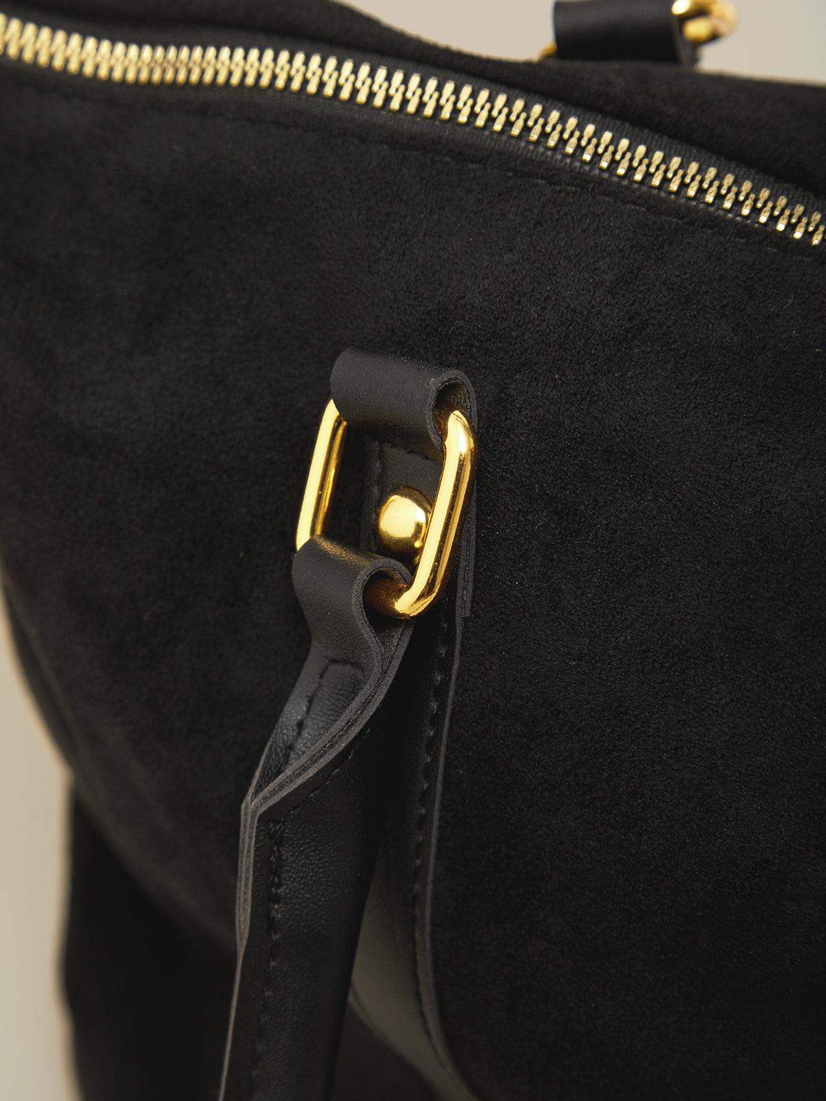 Black bag with gold zipper and clasp on a neutral background