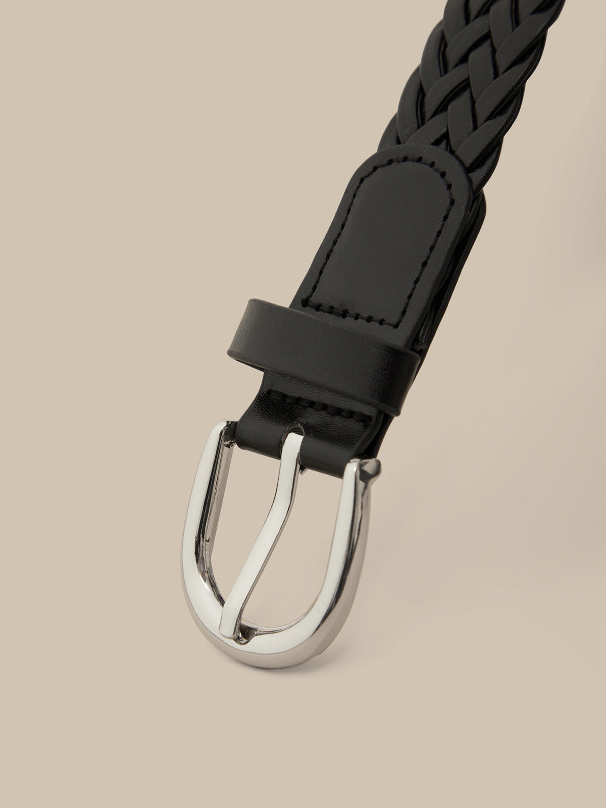 Black braided belt with silver buckle on a beige background