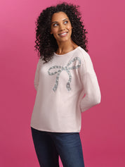 Woman wearing a light pink sweater with a green bow design on a purple background