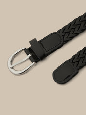 Black woven belt with silver buckle on a beige background