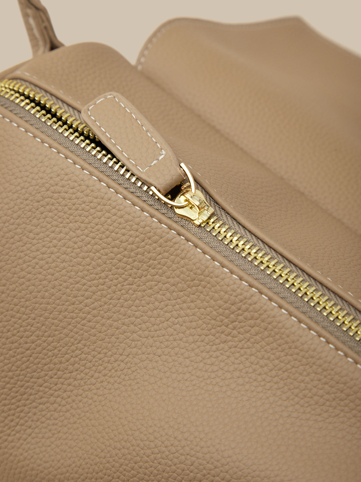 Close-up of a beige leather bag with a gold zipper.