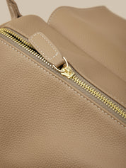 Close-up of a beige leather bag with a gold zipper.