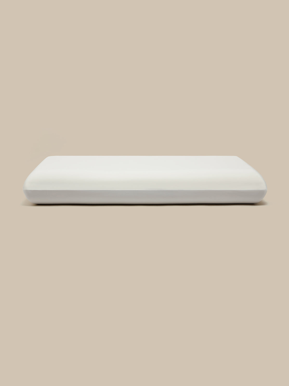 A white rectangular pillow with a smooth, matte finish, centered against a solid beige background.