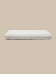 A white rectangular pillow with a smooth, matte finish, centered against a solid beige background.