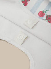 Close-up of a white garment with a button and a patterned background featuring red tomato and blue stripes.