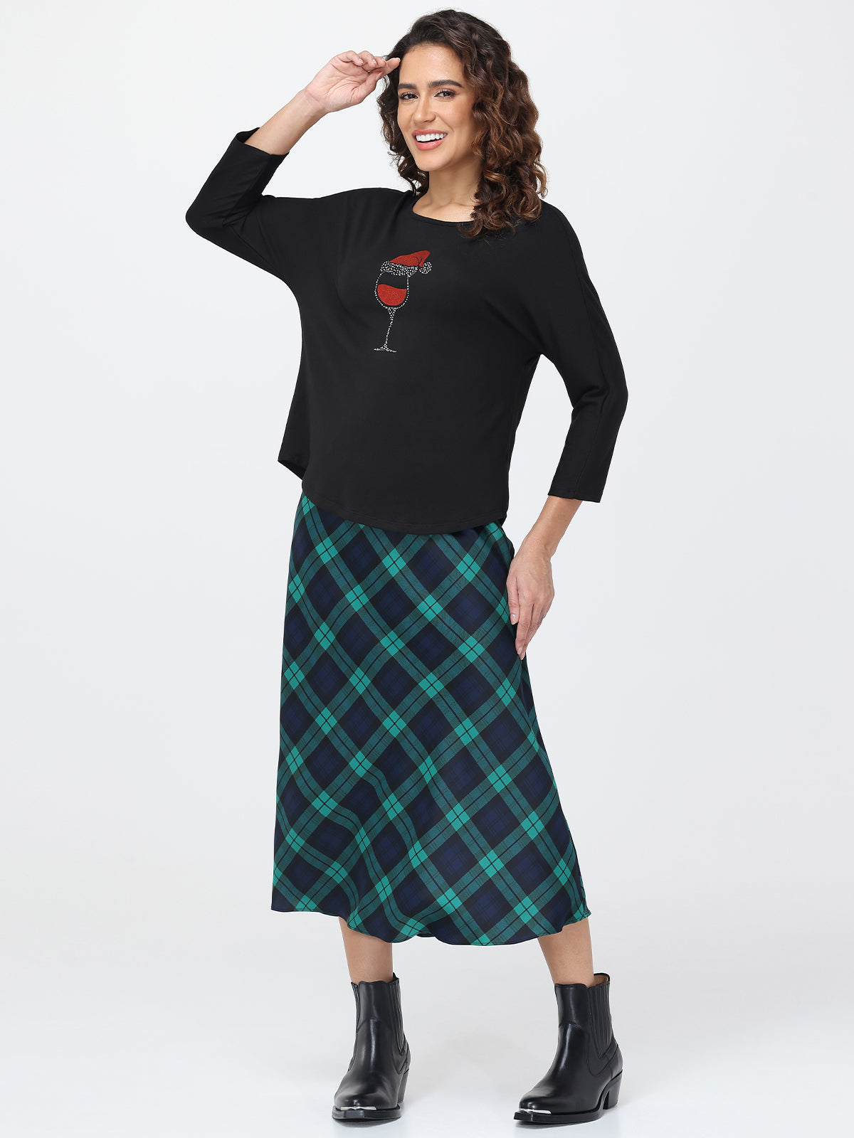 Woman wearing a black top with a graphic design and a green plaid skirt on a white background