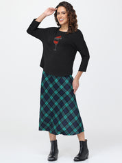 Woman wearing a black top with a graphic design and a green plaid skirt on a white background